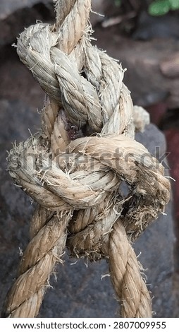 Close-up of rustic hemp rope tied in a knot on textured surface. Natural fiber rope with detailed weave and frayed texture. Marine and industrial concept.