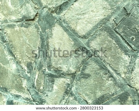 Close-up of a rustic natural stone wall with an irregular random pattern cladding in muted greenish-grey tones.