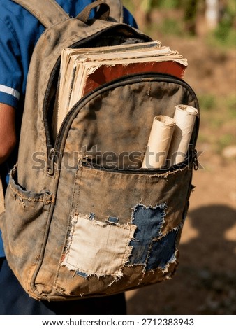 Close-up of a rustic, patched canvas backpack filled with worn, tattered books on the back of a rural student.