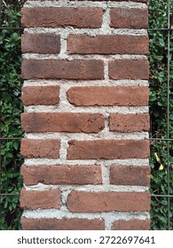 Close-up of a rustic red brick pillar with rough mortar texture against a green leaf background.