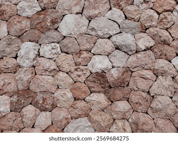 Close-up of a rustic stone wall. The wall is composed of irregularly shaped, natural stones in various shades of brown, grey, and beige. The stones are unevenly sized and fitted together.