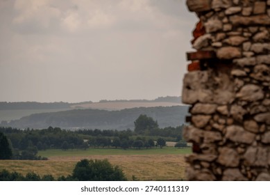 Close-up of a rustic stone wall overlooking a scenic landscape of rolling green hills and fields under a cloudy sky.