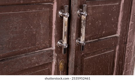 Close-up of a rustic wooden door with metal handles showing signs of wear and rust. The aged texture of the wood contrasts with the metallic sheen, creating a blend of vintage charm and industrial str - Powered by Shutterstock