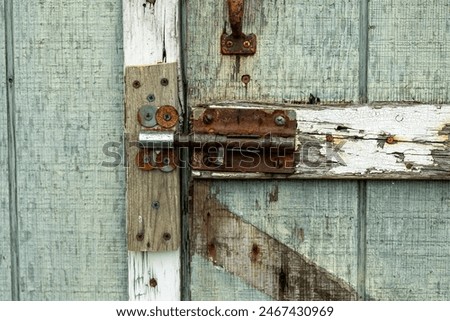 Close-up of a rusty bolt latch on an old, weathered wooden door, showcasing the beauty of rustic, vintage textures and decay over time.