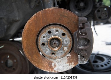 A Closeup Of A Rusty Disc Brake On A Junker Car, Wheel On The Ground In The Background