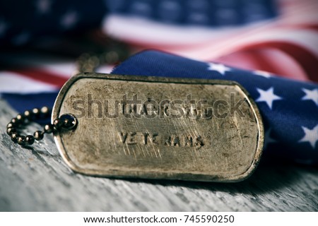 closeup of a rusty dog tag with the text thank you veterans engraved in it, next to a flag of the United States, on a rustic wooden surface