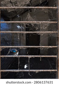 Close-up of rusty iron window bars with dusty spider webs inside an abandoned old building creating a spooky atmosphere.