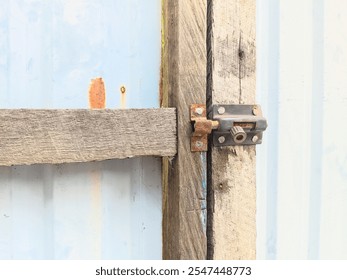 Closeup of a rusty metal latch on a weathered wooden gate affixed to a light blue corrugated metal surface. Shows age and wear. - Powered by Shutterstock