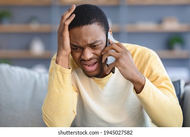 Closeup Of Sad Black Guy Sitting On Couch, Having Conversation On Mobile Phone, Touching His Head. Upset African American Young Man Talking On Smartphone, Fighting With Girlfriend