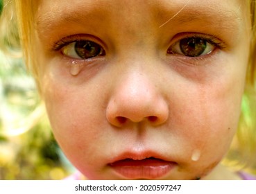 A close-up of a sad little girl with brown eyes crying with tears rolling down her face looking strait into your eyes- A little girl crying with tears in her eyes