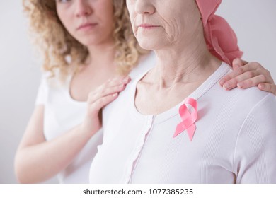 Close-up of sad senior woman with pink ribbon because of cancer supported by a caregiver - Powered by Shutterstock