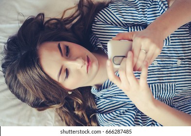 携帯電話を使ってベッドに横たわる10代の悲しい女の子の接写 携帯電話でメッセージを見たり 読んだり 電話を待ったりするのに退屈な表情をした若い美人 の写真素材 今すぐ編集