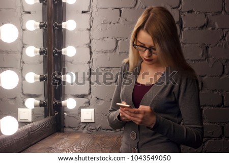 Closeup of sad teenage girl lying in bed using her mobile. Young pretty woman with bored expression looking at message on her cell phone, reading or waiting for call.