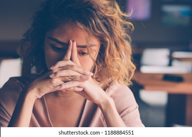 Closeup of sad young Asian woman at cafe leaning head on clasped hands and staring into vacancy. Tired freelancer feeling burnout. Stress and bad news concept