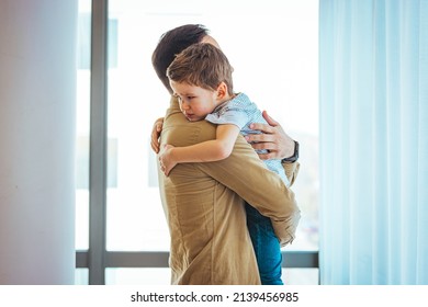 Closeup Sad Young Blond Boy Crying On Father Hands Indoor. Man Holds Son, Hugs And Comforts. Family Love, Care And Moral Support, Baby's Tears, Daddy's Arms. Dad Consoling Crying Child