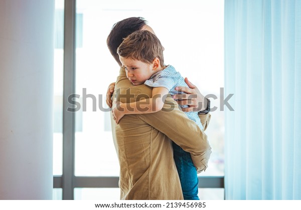 Closeup\
Sad young blond boy crying on father hands indoor. Man holds son,\
hugs and comforts. Family love, care and moral support, baby\'s\
tears, daddy\'s arms. Dad consoling crying\
child