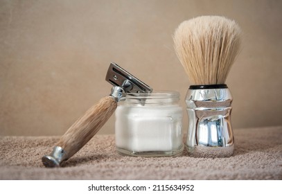 Close-up of safety razor 50s style and male cosmetic products and supplies used by men to shave. Safety razor, shaving brush and foam on beige towel background. Eco friendly tools for men shaving.