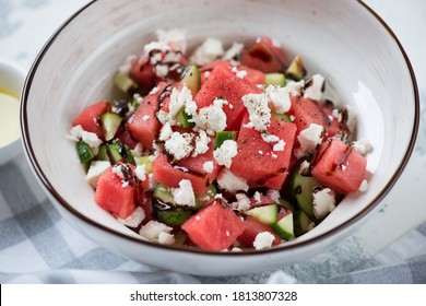 Close-up of salad with watermelon cubes, feta cheese, cucumber and balsamic sauce served in a white bowl, selective focus
