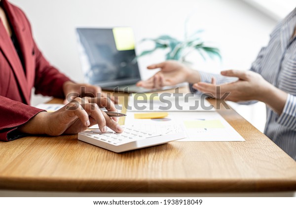 A close-up of the sales manager pressing the\
white calculator, she is examining the sales figures with\
management to summarize the monthly results and joint planning.\
Sales management concept.