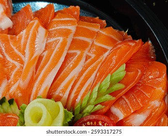 Close-up of salmon sashimi slices, arranged with garnishes on a dark plate.