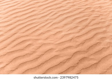 closeup of sand pattern of a beach in the summer. New trending PANTONE 13-1023 Peach Fuzz colour of 2024 year