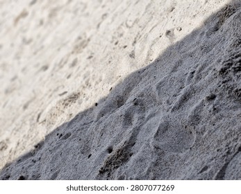 Close-up of sand texture divided into sunlit and shaded areas. High contrast natural background with direct sunlight and shadow split.