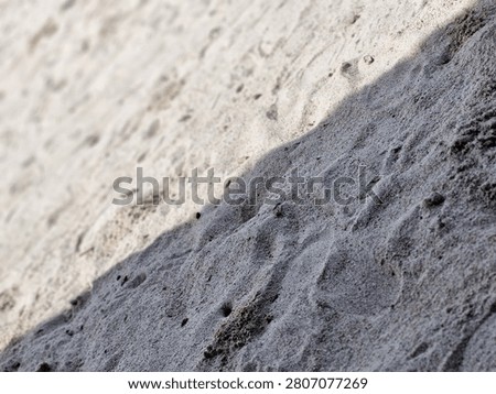 Close-up of sand texture divided into sunlit and shaded areas. High contrast natural background with direct sunlight and shadow split.
