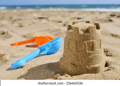 closeup of a sandcastle and toy shovels of different colors on the sand of a beach