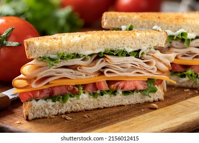 Closeup Of Sandwich Made With Sliced Turkey, Cheese , Lettuce And Tomato On Toasted Bread Cut In Half On A Cutting Board