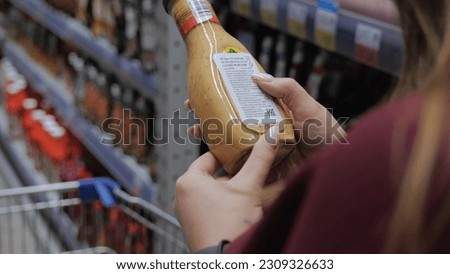 Close-up of a sauce bottle. A young woman reads the composition of the sauce. A girl in a supermarket buys sauce. hands close up. Translation: French salad dressing