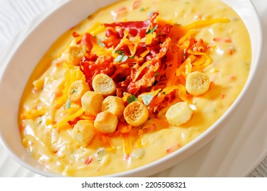 Close-up Of Savory Creamy Pumpkin Soup Topped With Fried Bacon, Shredded Cheddar Cheese And Salty Croutons In White Bowl On Wood Table