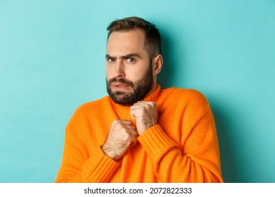 Close-up of scared bearded man looking startled and displeased, jumping from fear, standing over light blue background