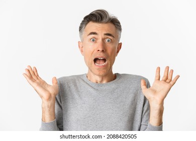 Close-up of scared middle-aged man, looking startled, jumping and screaming frightened, standing ambushed over white background
