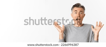 Close-up of scared middle-aged man, looking startled, jumping and screaming frightened, standing ambushed over white background.