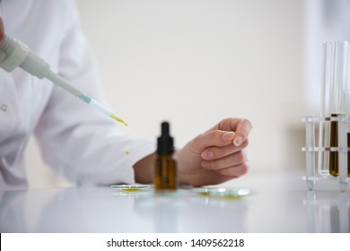 Closeup of scientist with a glasses testing cbd oil extracted from a marijuana plant on a watch glass. She is using a precise dropper and a watch glass for the experiment. Healthcare pharmacy concept