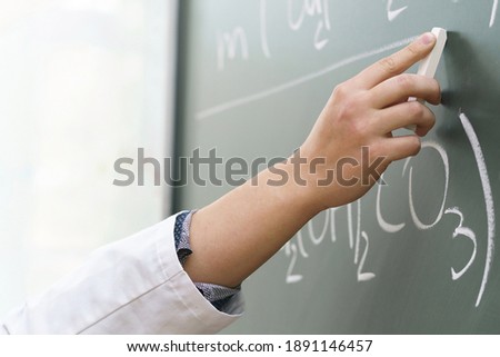 Closeup of scientist hand with a chalk writing a chemical equation
