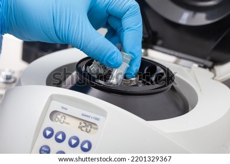 Closeup of a scientist hand placing a tube into an small table centrifuge. Spin column-based nucleic acid purification technique.