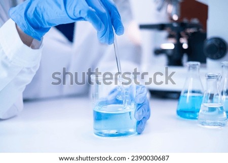 Closeup scientist hand using stirring rod for stirring blue liquid solution glass beaker chemical chemistry research science experiment test laboratory, scientific medicine technology lab analysis