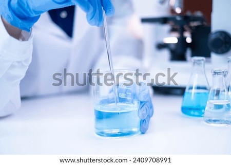 Closeup scientist hand using stirring rod for stirring blue liquid solution glass beaker chemical chemistry research science experiment test laboratory, scientific medicine technology lab analysis