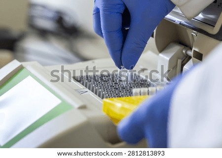 Close-up of a scientist holding a small Eppendorf tube containing a DNA sample in his fingers and placing it into a laboratory analyzer.
