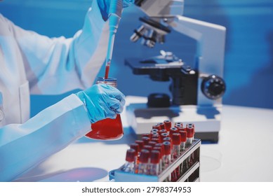 Close-up of a scientist using a precision pipette to drop orange liquid into a petri dish in a sterile laboratory environment.