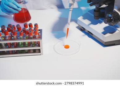 Close-up of a scientist using a precision pipette to drop orange liquid into a petri dish in a sterile laboratory environment.
