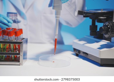 Close-up of a scientist using a precision pipette to drop orange liquid into a petri dish in a sterile laboratory environment.