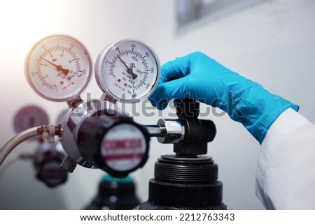 Closeup of a scientist's hand, checking gas from pressure gauge for a laboratory chromatography device during research.