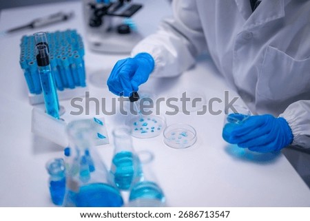 Closeup of scientist's hands using dropper to add blue liquid to petri dish in lab