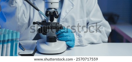 Close-up of scientist's hands using a microscope and pipette, conducting research and analysis in a modern laboratory setting with test tubes nearby