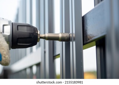 Close-up of screwing roofing screws into a metal picket fence. Installing the fence - Shutterstock ID 2155183981