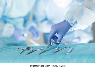 Close-up of scrub nurse taking medical instruments for operation with colleagues performing in background