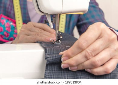 Closeup of seamstress hands working with clothing item on a sewing machine. Focus in the needle.