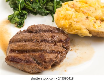 Closeup Of Seared Tenderloin Of Steak In Its Juices (au Jus) Served With Stuffed And Twice Baked Potato And Wilted Spinach.